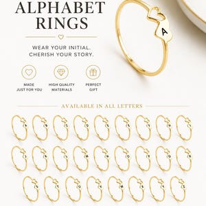 May include: A gold-toned ring featuring a heart-shaped charm with a black letter A. The image displays the text CUSTOM ALPHABET RINGS, WEAR YOUR INITIAL. CHERISH YOUR STORY, and shows a collection of rings with every letter from A to Z.