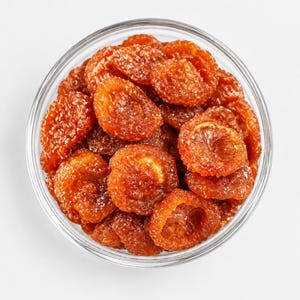 May include: A clear glass bowl filled with numerous dried, orange-colored fruit slices coated in a fine layer of granulated sugar. The pieces are round, textured, and translucent, showing a deep amber hue throughout the entire collection.