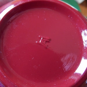 May include: Close-up of the bottom of a red ceramic mug with a small, embossed mark that reads "IF".