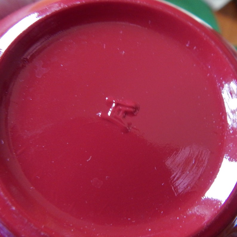 May include: Close-up of the bottom of a red ceramic mug with a small, embossed mark that reads "IF".