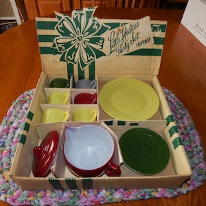 May include: A vintage Little Hostess Party Set in a cardboard box with a green and white striped design. The set includes a teapot, cups, saucers, and a plate. The box is open and the set is visible inside.