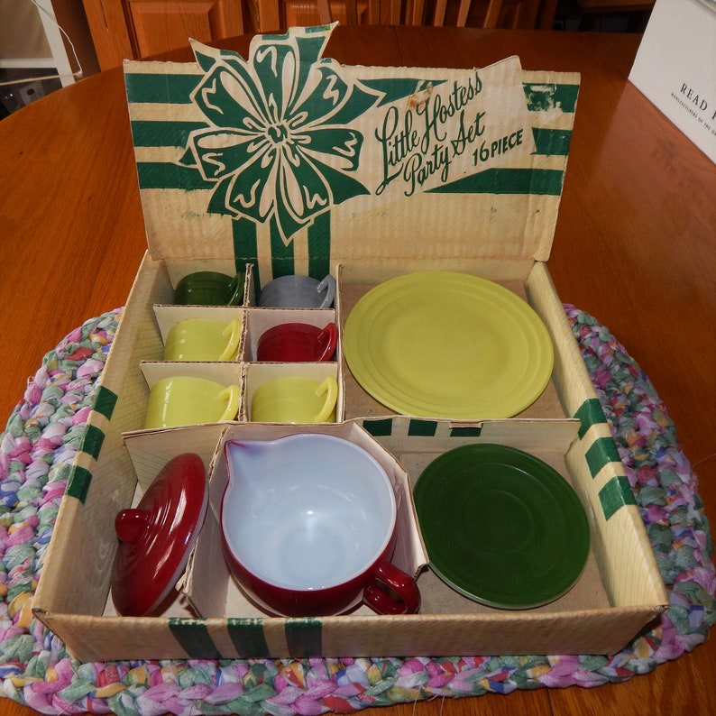 May include: A vintage Little Hostess Party Set in a cardboard box with a green and white striped design. The set includes a teapot, cups, saucers, and a plate. The box is open and the set is visible inside.