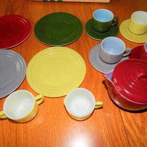 May include: A vintage children's tea set with a red teapot, yellow, green, and gray plates, and cups in various colors, including yellow, blue, and purple.