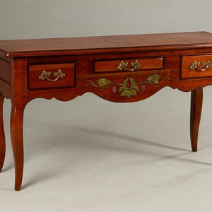 May include: A reddish-brown wooden console table with three drawers, each with brass handles. The table has a decorative vine and grape design and curved legs. The table's measurements are in centimeters.