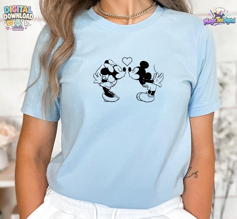 May include: A light blue short-sleeve t-shirt featuring a black graphic print of two cartoon mice kissing with a small heart positioned between them. The shirt has a crew neckline and a simple, clean design on the front center of the garment.