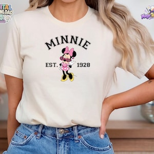 May include: A cream-colored short-sleeve t-shirt featuring a graphic of Minnie Mouse wearing pink sunglasses and a pink polka dot dress. The text "MINNIE" is arched above the character, with "EST. 1928" printed horizontally on either side.