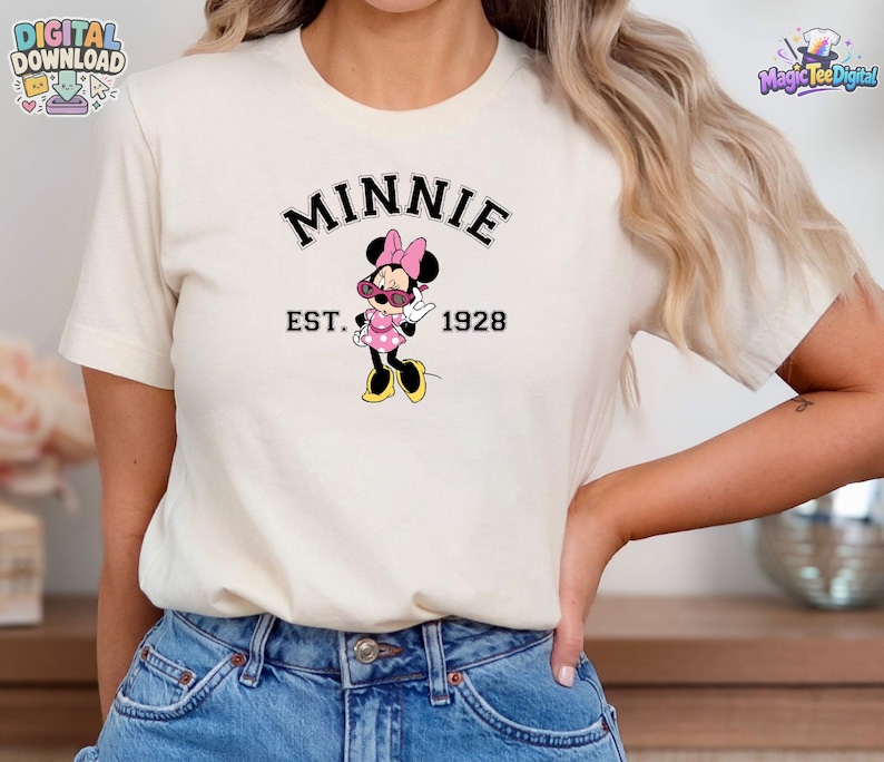 May include: A cream-colored short-sleeve t-shirt featuring a graphic of Minnie Mouse wearing pink sunglasses and a pink polka dot dress. The text "MINNIE" is arched above the character, with "EST. 1928" printed horizontally on either side.