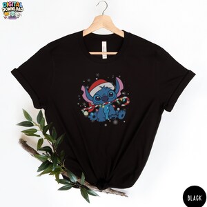 May include: Black t-shirt featuring a cartoon character wearing a Santa hat and holding a candy cane. The character is blue with large eyes and is surrounded by snowflakes. The shirt has the text "DIGITAL DOWNLOAD" at the top.