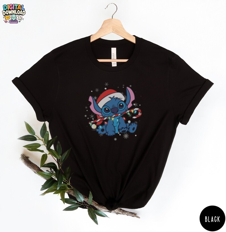 May include: Black t-shirt featuring a cartoon character wearing a Santa hat and holding a candy cane. The character is blue with large eyes and is surrounded by snowflakes. The shirt has the text "DIGITAL DOWNLOAD" at the top.