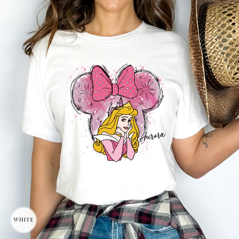 May include: White t-shirt with a pink Minnie Mouse-shaped design, a polka dot bow, and a princess illustration. The word "Aurora" is written in cursive. The shirt has a classic crew neck.