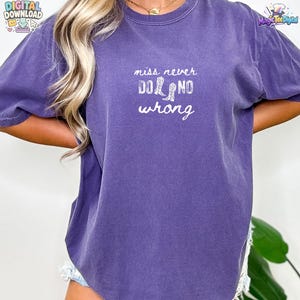 May include: A purple short-sleeve t-shirt featuring white text that reads miss never DO NO wrong, with the word DO replaced by two white cowboy boot illustrations. The shirt has a crew neckline and a relaxed fit with a slightly faded fabric texture.
