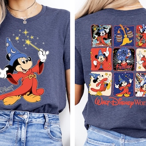 May include: Heather navy blue t-shirt featuring a graphic of Mickey Mouse as a sorcerer with a wand and stars. The back of the shirt displays Mickey Mouse in various poses with the words "Walt Disney World".