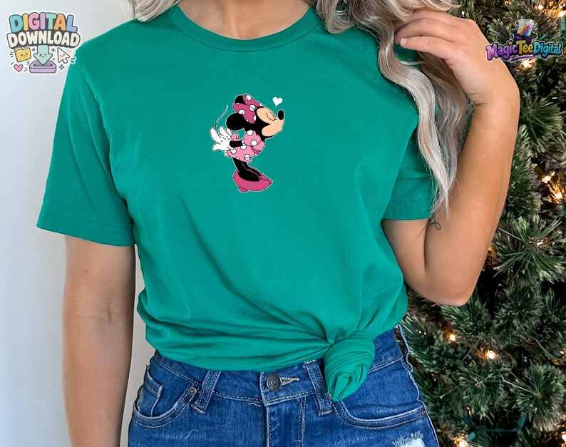 May include: A bright green short-sleeved t-shirt featuring a centered graphic of Minnie Mouse wearing a pink polka-dot dress and bow, blowing a kiss with a small white heart above her head. The shirt is paired with blue denim jeans.