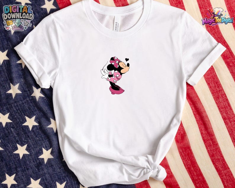 May include: A white short-sleeved crew neck t-shirt featuring a small graphic of Minnie Mouse in a pink polka-dot dress and bow, blowing a kiss with a small black heart icon above her head. The shirt has a simple, clean design on the front.