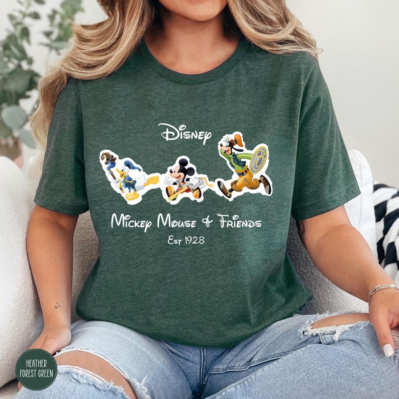 May include: Heather forest green t-shirt featuring a graphic of Mickey Mouse and Friends. The design includes Disney's logo and the text "Mickey Mouse & Friends Est 1928". The cartoon characters are in motion, with Mickey Mouse in the center.
