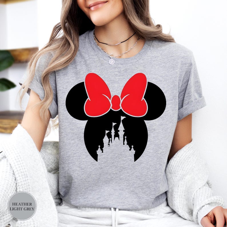 May include: Heather light grey t-shirt featuring a black silhouette of a mouse head with a red bow and a castle design. The text "Heather Light Grey" is printed on the bottom left of the shirt.