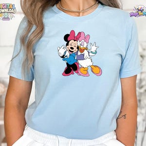 K&ouml;nnte beinhalten: Ein hellblaues kurz&auml;rmeliges T-Shirt mit einem Grafikdruck von Minnie Maus und Daisy Duck, die nebeneinander stehen. Minnie tr&auml;gt ein blaues Kleid und eine rosa Schleife, w&auml;hrend Daisy ein violettes Oberteil, eine rosa Schleife und rosa Schuhe tr&auml;gt.