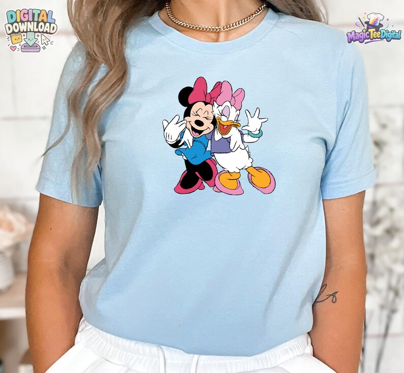 K&ouml;nnte beinhalten: Ein hellblaues kurz&auml;rmeliges T-Shirt mit einem Grafikdruck von Minnie Maus und Daisy Duck, die nebeneinander stehen. Minnie tr&auml;gt ein blaues Kleid und eine rosa Schleife, w&auml;hrend Daisy ein violettes Oberteil, eine rosa Schleife und rosa Schuhe tr&auml;gt.