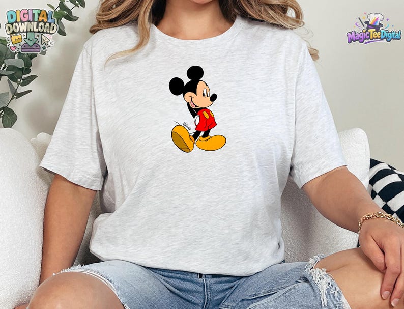 Peut inclure: Un t-shirt &agrave; manches courtes gris chin&eacute; clair avec un motif central repr&eacute;sentant Mickey Mouse. Le personnage est illustr&eacute; dans une pose classique, portant un short rouge et de grandes chaussures jaunes, avec le logo Disney en noir.
