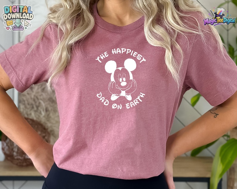 Puede incluir: Una camiseta de manga corta de color malva con un gr&aacute;fico blanco de Mickey Mouse y el texto "THE HAPPIEST DAD ON EARTH" impreso en disposici&oacute;n circular alrededor del personaje. La camiseta tiene cuello redondo y corte est&aacute;ndar.