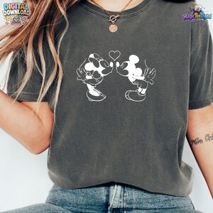 May include: A charcoal gray short-sleeve t-shirt featuring a white line art graphic of two cartoon mice leaning toward each other with a small heart positioned between their heads. The shirt has a crew neckline and a vintage-style washed finish.
