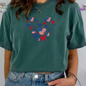 Puede incluir: Una camiseta de manga corta de color verde oscuro con un gr&aacute;fico central compuesto por varias siluetas peque&ntilde;as de orejas de rat&oacute;n en rojo, blanco y azul, con algunos patrones que recuerdan a la bandera estadounidense, combinada con vaqueros azules.