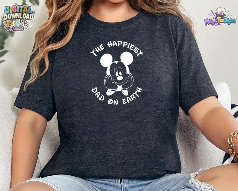 Puede incluir: Una camiseta de manga corta en gris jaspeado oscuro con un gr&aacute;fico blanco de una cabeza de rat&oacute;n de dibujos animados con las manos apoyadas en las mejillas. El texto "THE HAPPIEST DAD ON EARTH" est&aacute; impreso en blanco en arco.