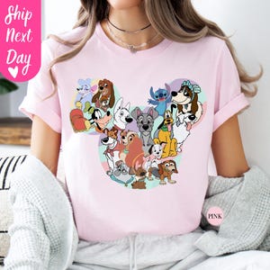 May include: Pink t-shirt featuring a Mickey Mouse-shaped design filled with various cartoon dog characters. The shirt has short sleeves and the text "Ship Next Day" is visible on the left side. The word "Pink" is also visible on the right side.