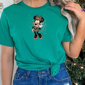 May include: A bright green short-sleeved t-shirt featuring a central graphic of a cartoon mouse character wearing a leopard print outfit, a matching bow, and pink-tinted glasses, surrounded by small copper-coloured glitter-like speckles.