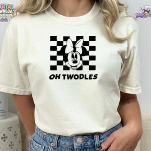 May include: A cream-coloured short-sleeve t-shirt featuring a black graphic of a cartoon mouse head with a bow centred over a black and white checkered square pattern. The text OH TWODLES is printed in black capital letters below the graphic.