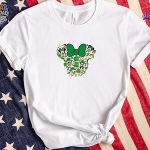 Pu&ograve; includere: Una t-shirt bianca a maniche corte con una grafica centrale a forma di silhouette di testa di topo. Il design &egrave; riempito con icone verdi a tema San Patrizio, tra cui trifogli, cappelli da leprecano, pentole d'oro e volti di personaggi.