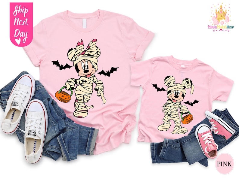 May include: Pink t-shirts featuring a mummy-themed Minnie Mouse and Mickey Mouse design, holding jack-o'-lanterns, with black bat silhouettes. The shirts are paired with blue jeans and white sneakers. The text "Ship Next Day" is visible.
