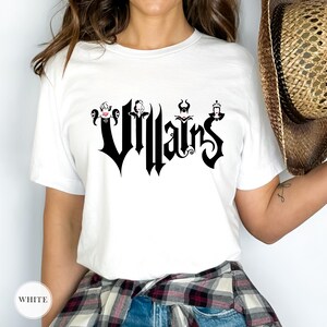 May include: White t-shirt featuring the word "Villains" in a gothic font, with stylized character illustrations above each letter. The shirt is a classic crew neck style.