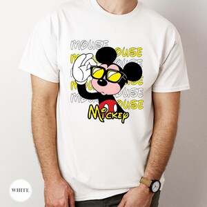 May include: White t-shirt featuring a cartoon Mickey Mouse character wearing yellow sunglasses. The design includes the word "MOUSE" in a repeating pattern and the name "Mickey" in yellow. The shirt is a classic crew neck.