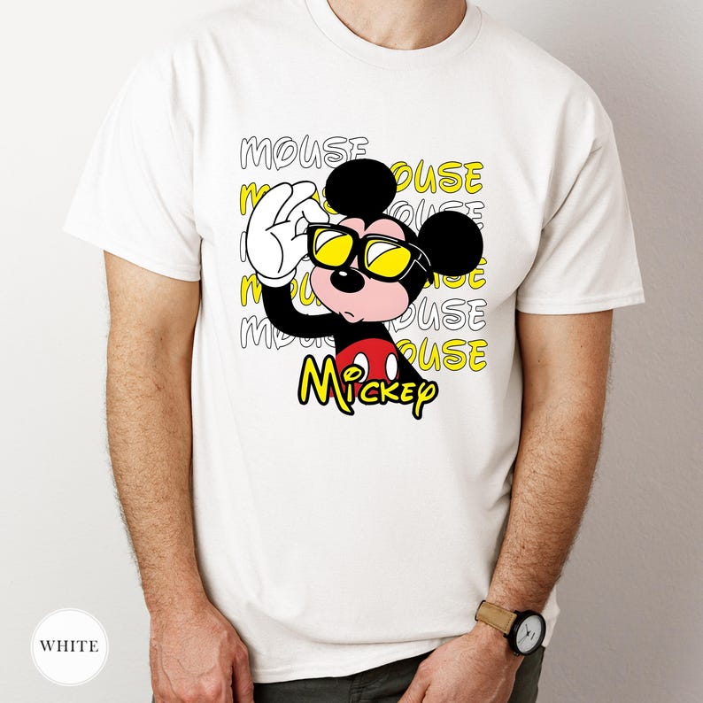 May include: White t-shirt featuring a cartoon Mickey Mouse character wearing yellow sunglasses. The design includes the word "MOUSE" in a repeating pattern and the name "Mickey" in yellow. The shirt is a classic crew neck.