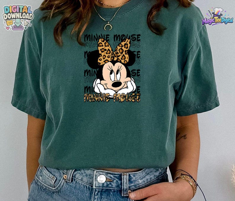 Pode incluir: Uma t-shirt de manga curta verde-azulado escuro com um gr&aacute;fico da Minnie Mouse com um la&ccedil;o de estampa de leopardo. O design inclui o texto "MINNIE MOUSE" repetido no fundo e impresso em estampa de leopardo na parte inferior.