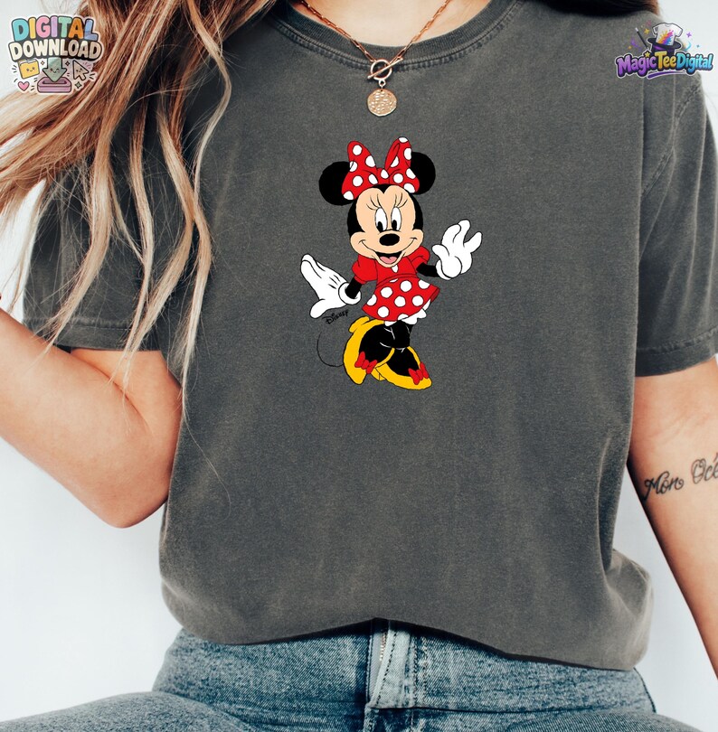 Peut inclure: Un t-shirt gris anthracite &agrave; manches courtes avec une impression graphique de Minnie Mouse portant une robe rouge &agrave; pois blancs, un n&oelig;ud rouge assorti et des chaussures jaunes. Le personnage est plac&eacute; au centre du v&ecirc;tement.