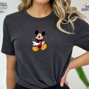 May include: A dark heather gray short-sleeve t-shirt featuring a centered graphic of Mickey Mouse. The character is depicted with a smiling expression, wearing red shorts and yellow shoes, surrounded by small red hearts floating above the head.