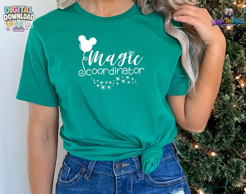 May include: A kelly green short-sleeve t-shirt featuring a white graphic print of a mouse-ear balloon and the text "magic coordinator" in a cursive font, accompanied by a trail of small sparkling stars below the lettering.