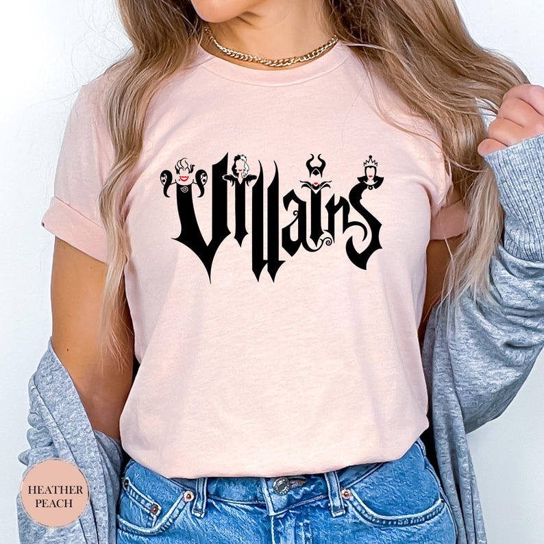 May include: Heather peach-colored t-shirt with the word "Villains" in a gothic font. The word is in black and features silhouettes of Disney villains. The shirt is a short-sleeved crew neck.