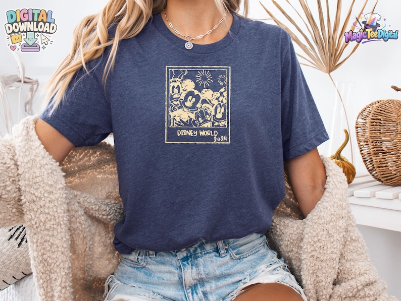 K&ouml;nnte beinhalten: Ein kurz&auml;rmeliges T-Shirt in meliertem Marineblau mit einem cremefarbenen Grafikdruck eines Polaroid-Rahmens, der Disney-Figuren und Feuerwerk zeigt, mit dem deutlich lesbaren Text "DISNEY WORLD 2024" am unteren Rand des Rahmens.