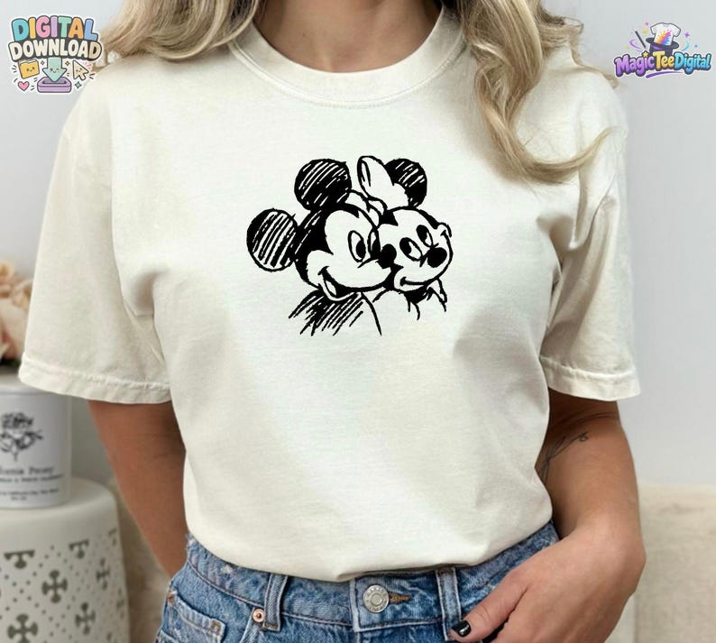 May include: A cream-colored short-sleeve t-shirt featuring a black ink-style sketch graphic of two cartoon mice heads positioned side-by-side on the chest. The design uses hatched lines to create the character features and outlines.
