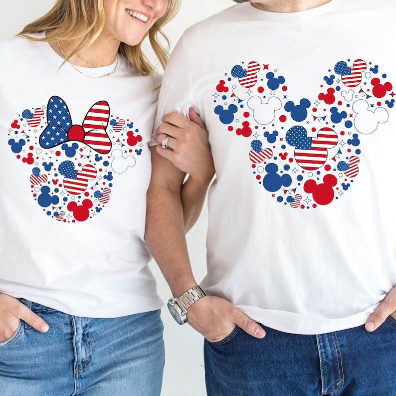 May include: White t-shirts featuring a Mickey Mouse head design composed of red, white, and blue shapes and patterns. One shirt has a Minnie Mouse bow. The shirts are worn with blue jeans.