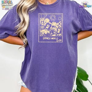 K&ouml;nnte beinhalten: Ein violettes Kurzarm-T-Shirt mit einem rechteckigen, hellgelben Grafikdruck. Das Motiv zeigt Zeichentrickfiguren wie Mickey Maus, Minnie Maus, Donald Duck und Goofy, darunter steht der Text Disney World 2024.
