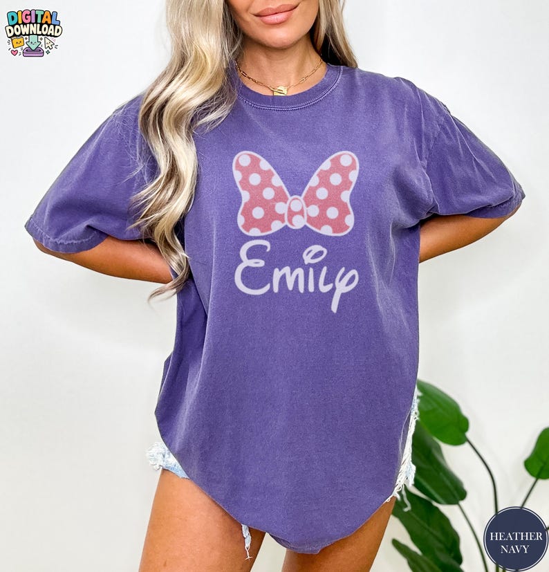 May include: A purple t-shirt featuring a pink polka-dot bow and the name "Emily" in white script. The shirt has short sleeves and a relaxed fit. The words "Digital Download" are in the top left corner.