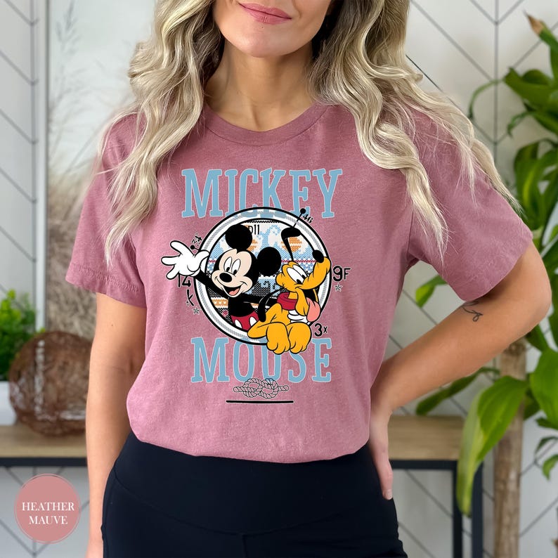May include: Heather mauve t-shirt featuring a circular graphic with Mickey Mouse and Pluto. The graphic includes the words "Mickey Mouse" in light blue. The shirt is a short-sleeved crew neck.