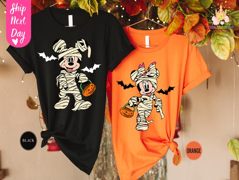 May include: Black and orange Halloween t-shirts featuring Mickey and Minnie Mouse dressed as mummies, holding jack-o'-lanterns. White bats are printed above the characters. The text "Ship Next Day" is visible on the left side of the image.