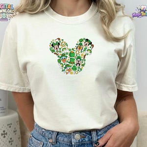 Pu&ograve; includere: Una t-shirt a maniche corte color crema con un design grafico centrale composto da vari personaggi dei cartoni animati e simboli del giorno di San Patrizio disposti a forma di silhouette di testa di topo, inclusi cappelli verdi e trifogli.