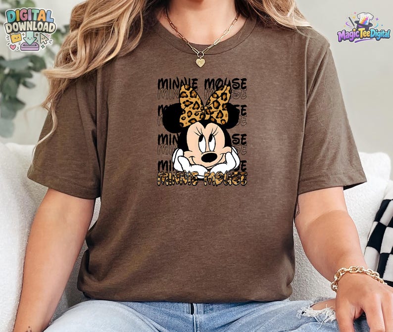 Pode incluir: Uma t-shirt castanha de manga curta com um gr&aacute;fico da Minnie Mouse com um la&ccedil;o de estampado de leopardo. O texto "MINNIE MOUSE" &eacute; repetido no fundo e impresso com um padr&atilde;o de leopardo na parte inferior do design gr&aacute;fico frontal.