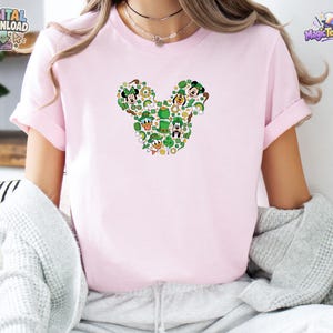 Pu&ograve; includere: Una t-shirt a maniche corte color rosa chiaro con una grafica centrale a forma di silhouette di testa di topo. La grafica &egrave; composta da varie icone verdi a tema San Patrizio, tra cui trifogli, leprecauni e volti di personaggi animati.